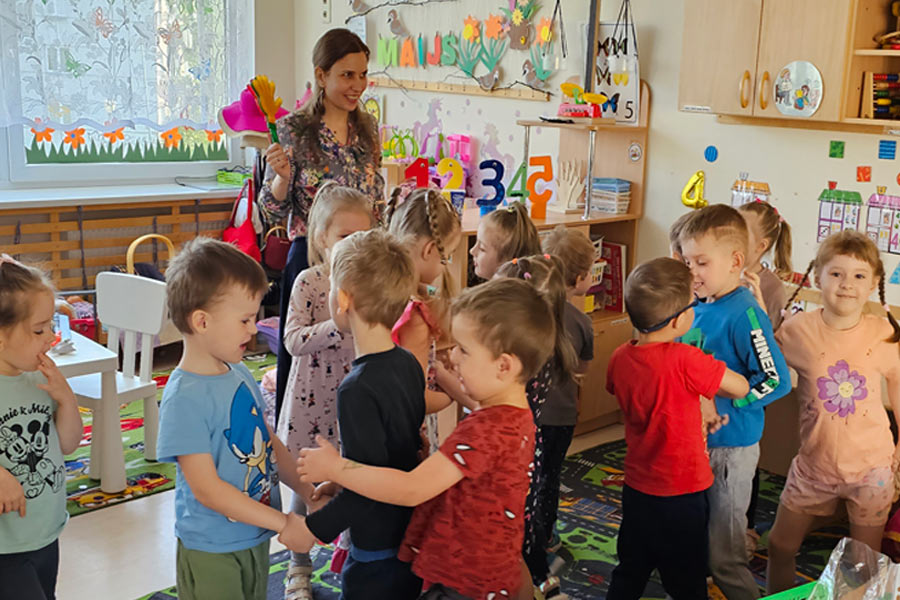 Daudz bērnu iekštelpās veic vingrinājumus skolotāja vadībā